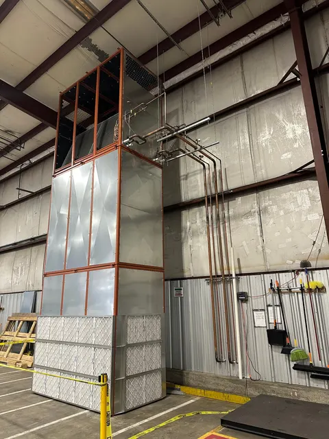 Tall commercial air-handling equipment with filters, metal panels and adjacent pipework inside an industrial building.