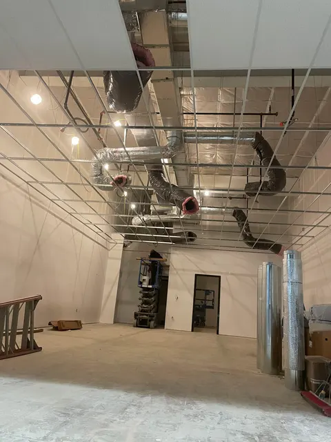 Metal ductwork and insulated branches above an open ceiling grid in an unfinished commercial interior.