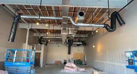 Metal supply ductwork and insulated flexible branches suspended from exposed framing in a commercial space.