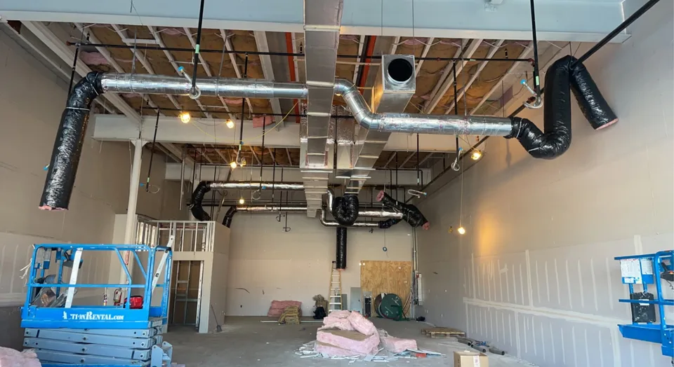 Metal supply ductwork and insulated flexible branches suspended from exposed framing in a commercial space.