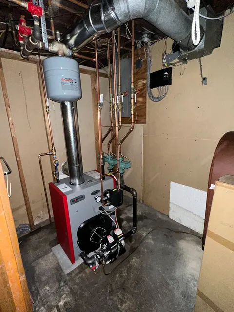 Floor-mounted oil-fired boiler with an expansion tank, circulation pumps and overhead heating-zone pipework.